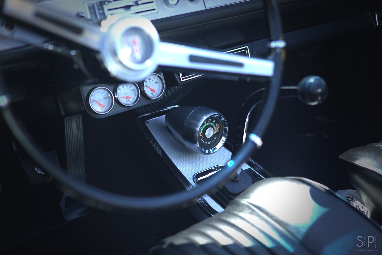 Color photo of a classic car interior with steering wheel and gauges.
